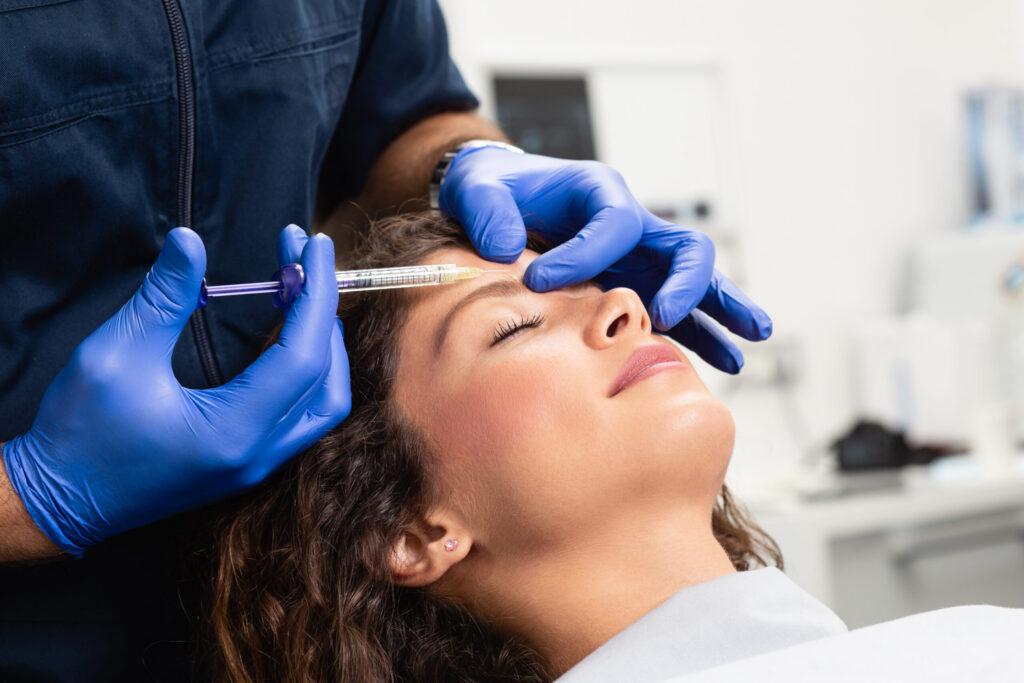 Medical professional in blue gloves administers an injection to a patient’s forehead in a clinical setting, patient with eyes closed.