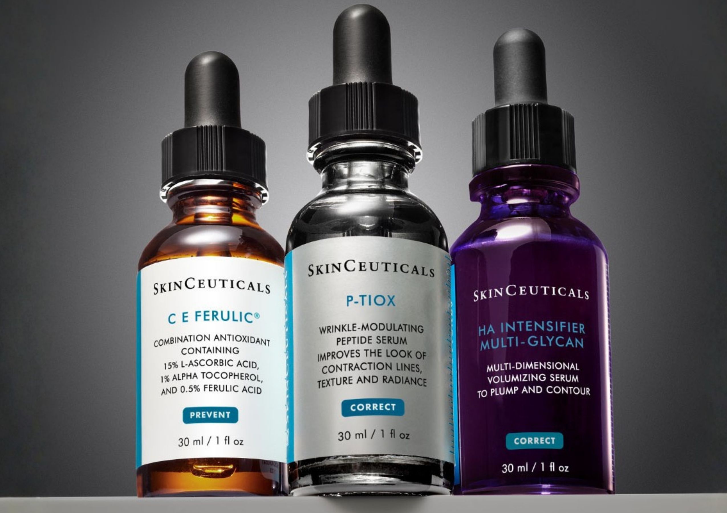 Three SkinCeuticals serum bottles with dropper tops, containing orange, clear, and purple liquids, arranged in a row on a gray background.